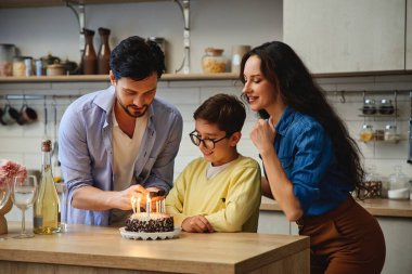 Bir çocuk doğum günü dileği diler ve ebeveynler pastayı mumlarla yakar..