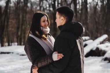 Karlı bir orman ortamında gülümseyen ve kucaklaşan iki insan
