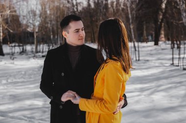 Ağaçlarla çevrili karlı bir arazide iki insan romantik bir anı paylaşıyor..