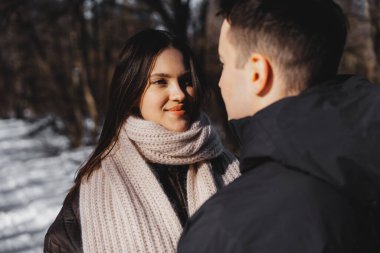 Genç çift, karlı bir arazide birbirlerine yakın duruyorlar, gülümsüyorlar..
