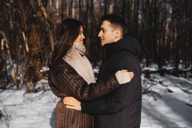 Karlı bir ormanda güneş ışığıyla samimi bir anı paylaşan iki insan..