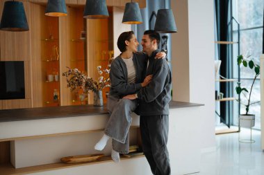 Çift şık bir mutfakta kucaklaşır, birlikte neşeli bir anı paylaşır..