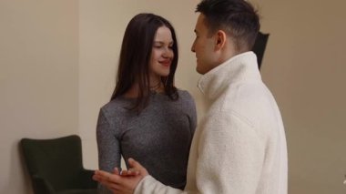 Bir çift, sıcak bir odada, karşılıklı gülümseme ve neşe içinde, yakın bir dansın tadını çıkarır..