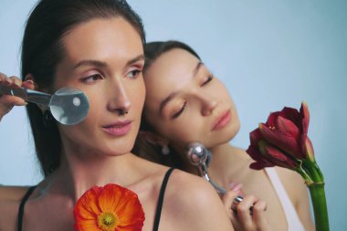 İki kadın çiçek elementleri ve aletleri içeren bir güzellik rutini uyguluyor..