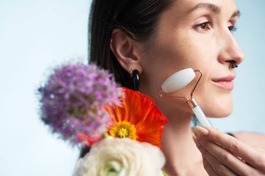 Renkli çiçeklerle çevrili bir kadın yüzüne yeşim bir silindir takıyor..