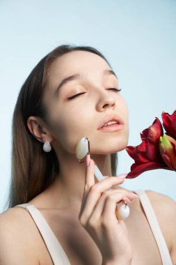 Genç bir kadın güzellik aleti ve çiçekle cilt bakımını seviyor..