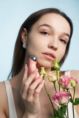 Kadın, taze çiçekleri sergilerken güzellik cihazıyla etkileşime girer..