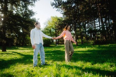 Güneşli, yemyeşil bir parkta el ele tutuşan çift..