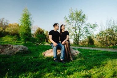 Sevimli bir çift, canlı yeşilliklerle çevrili büyük bir kayanın üzerinde birlikte otururlar..