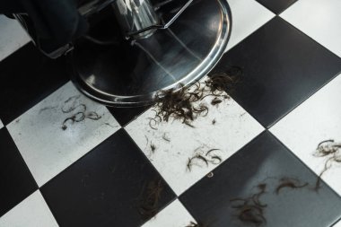 Siyah beyaz kareli zemin, saç tıraşından sonra budanmış saçlarla dolu..