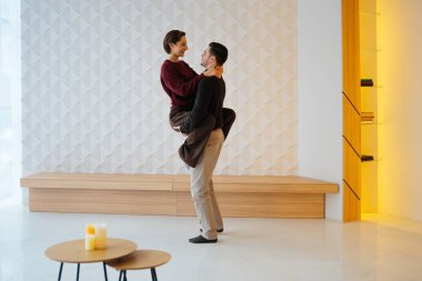 Çift şık bir iç mekanda dururken sevgi dolu bir kucaklaşmayı paylaşır..