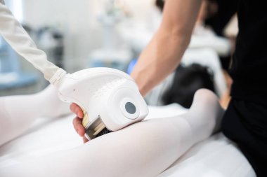 Sağlık uzmanı, klinikte tedavi için hastaların bacakları üzerinde cihaz kullanıyor.