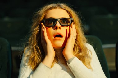 Kadın sinemada şaşkınlığını ifade ederken film sırasında 3D gözlük takıyor..