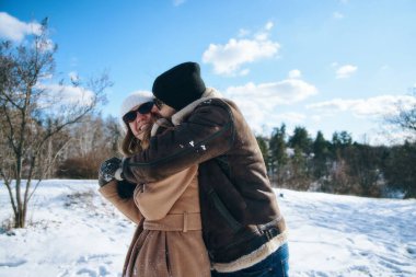 İki insan karda eğleniyor, kışın kucaklaşıp gülümsüyor..