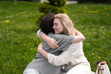 Çevrelerinde canlı yeşilliklerle çevrili iki kadın mutlu bir şekilde birbirine sarılıyor..