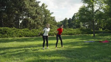 Arkadaşlar yeşil bir parkta güneşlenirken birlikte spor yapıyorlar..