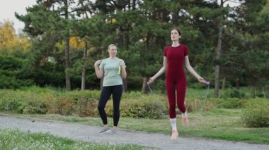 İki kadın güneşli bir parkta ip atlama alıştırması yapıyor, spor ve koordinasyon üzerine odaklanıyorlar..