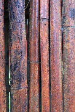 Yıpranmış bambu direklerinin yakın çekimlerinde turuncu ve siyah tonlarıyla kırsal bir doku sergileniyor..