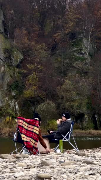秋の山間の川でお茶を飲みピザハイキングのコンセプトで椅子に座って — ストック動画