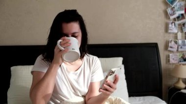 Kadın yatakta çay içiyor. Sabah ayininde haberleri kontrol ediyor.