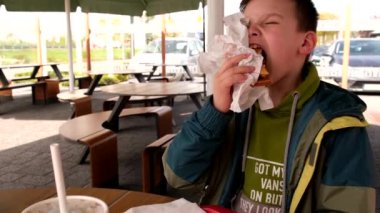 7 yaşında bir çocuk kafede çizburger yiyor.
