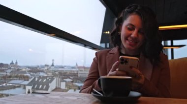 Mutlu, çay içen güzel bir kadın arka planda Lviv şehrinde sosyal ağları kontrol ediyor.