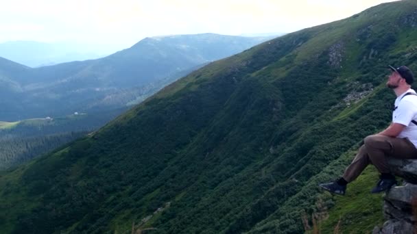 カルパチア山脈の風景を楽しむ崖の上に座っている男ハイカーコピースペースウクライナ — ストック動画