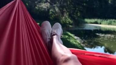 woman laying down on hammock at sunny day legs in white sneakers swinging