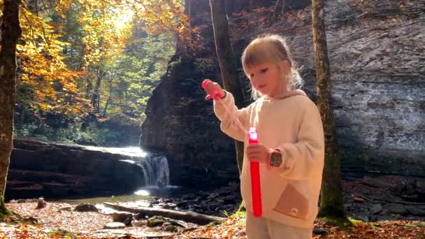 幸せな女の子作る石鹸泡屋外で遊ぶ秋の森の滝を背景に — ストック動画