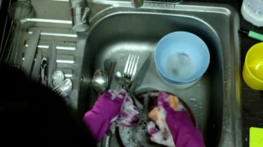 Lastik eldivenli bir kadın mutfak lavabosunda bulaşık yıkıyor.