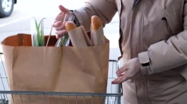 Bir adam market arabasının bagajına alışveriş poşeti koyar.