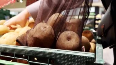 Kadın, markette torbaya patates koydu. Yakından.