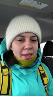 Kadın, kamerada selfie çekiyor. Kış kıyafetiyle arabada oturuyor.