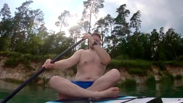 男人坐在船板上 在清澈的湖水上划船 — 图库视频影像