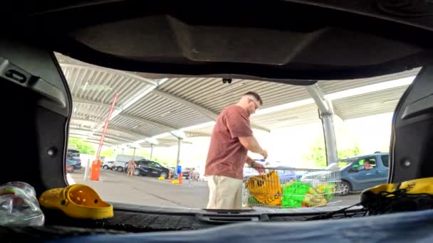 男は食料品店の駐車場のライフスタイルで車のトランクにパッケージを置きました — ストック動画