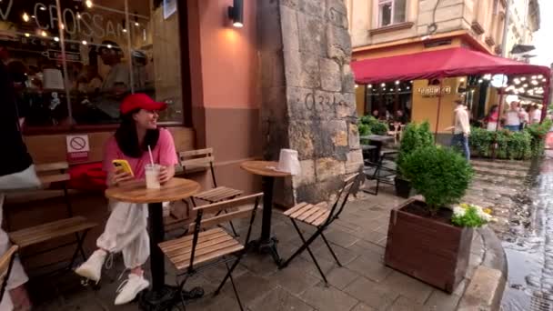 外面的咖啡店里 有一个女人在一边喝酒一边吃羊角面包 一边打电话上网 — 图库视频影像