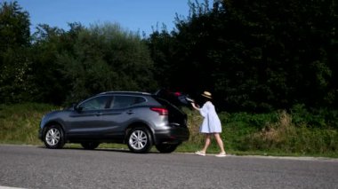 Mutlu güzel kadın çantayı arabanın bagajına koydu. Dışarıdan görüntüyü kapatıyor.