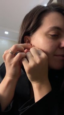 Güzel bir kadın randevuya hazırlanırken küpelerini takar. Yakın plan.