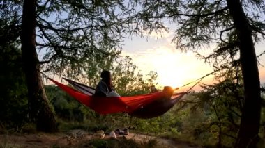 Ormanda gün batımında hamakta bir adamla bir kadın