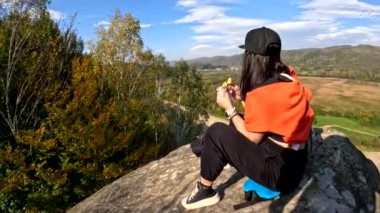 Mutlu kadın yürüyüşçü kayanın tepesinde, hamburger yiyor sonbahar sezonunun tadını çıkarıyor.