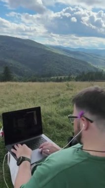 Dağın tepesinde dizüstü bilgisayarı olan bir adam serbest dağcılık konseptinde çalışıyor.