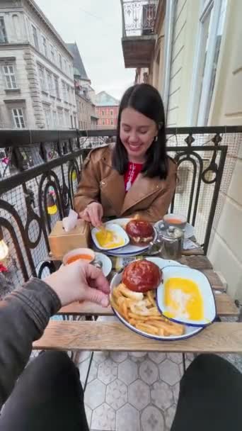 一对快乐的夫妇在可爱的欧洲城市外的阳台边的咖啡店里吃汉堡包 — 图库视频影像