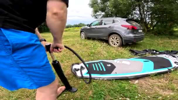 男はビーチの夏の活動で車の近くでスーパーボードを膨らませる — ストック動画