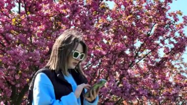 Diş teli takan kadın telefonda selfie çekiyor arka planda sakura açıyor.