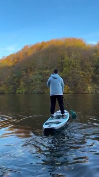 秋の湖の真ん中にあるスーパーボードの男の景色 背景にカラフルな森 — ストック動画