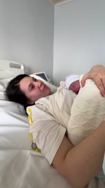 Kadın hastane yatağında, yeni doğan oğluna sarılıyor. Annelik mutluluğu.