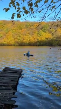 Sonbahar Gölü 'nün ortasında arka planda renkli ormandaki insan manzarası