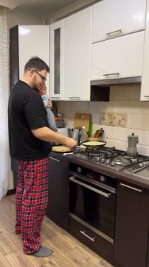 Modern bir mutfakta yemek hazırlayan bir adam bebeğini elinde tutuyor.