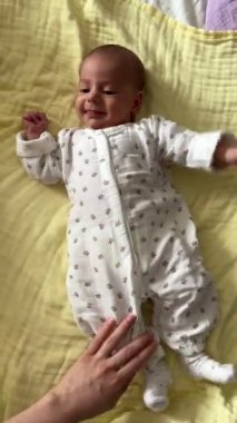 Bebek sarı battaniyeye uzanmış, annesinin elini tutuyor.