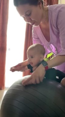 Anne, erkek bebekle topa uygun annelik egzersizi yapar.